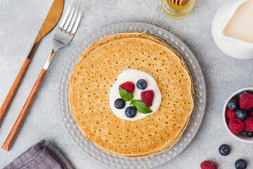 Plate of delicious thin pancakes with berries on grey table Copy space.