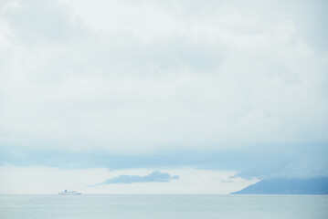 Fototapeta na wymiar alone marine cruise ship on horizon with dramatic morning foggy sky, sea and mountain landscape background, horizontal stock photo image backdrop
