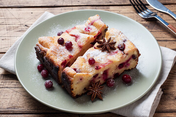 Two pieces of cottage cheese pie casserole with cranberry berries and spices cinnamon and anise on a plate. Wooden background.