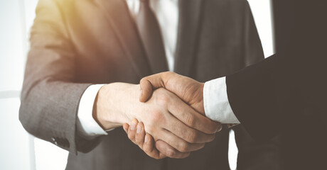 Obraz premium Unknown diverse business people are shaking hands finishing contract signing in sunny office, close-up. Business handshake concept