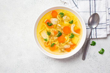 Homemade chicken soup with noodles and vegetables in white bowl, white background, top view.