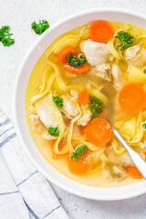 Homemade chicken soup with noodles and vegetables in white bowl, white background, top view.