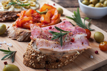 Wholegrain bread sandwiches with cream cheese, bacon and olives canned peppers with tomato on wooden background.