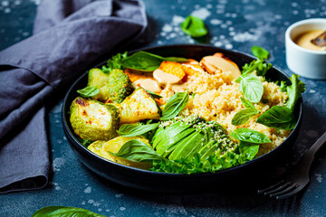 Vegan lunch plate. Quinoa salad with baked zucchini, sweet potato, avocado and tahini dressing in black plate, dark background.