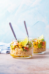 Vegan salad with vegetables and quinoa in glass jars, blue background.