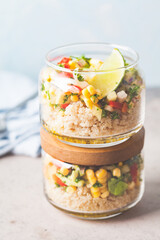 Vegan salad with vegetables and quinoa in glass jars, blue background.