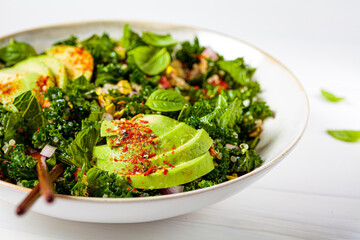 Healthy salad with kale, quinoa, nuts and avocado in white bowl. Healthy vegan food concept.