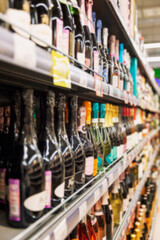 Rows of bottles of alcohol on the shelves in the supermarket. Vertical. Blurred.