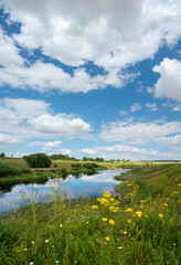 Summer rural landscape with calm river and beautiful clouds in blue sky.