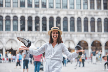 woman in white clothes with straw hat having fun with pigeons at venice city square