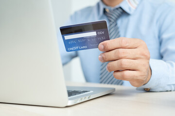 The businessman's hand is holding a credit card and using a laptop for online shopping and internet payment in the office