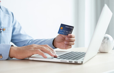 The businessman's hand is holding a credit card and using a laptop for online shopping and internet payment in the office