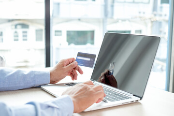 The businessman's hand is holding a credit card and using a laptop for online shopping and internet payment in the office