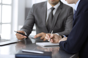 Unknown businessman using tablet computer and working together with his colleague while sits at the glass desk in modern office. Teamwork and partnership concept