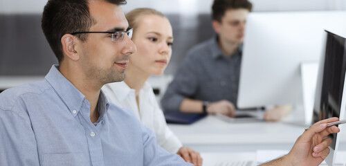 Business people working together in modern office. Happy smiling adult businessman using pc computer with colleagues. Teamwork and partnership concept