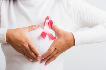 Breast cancer awareness healthcare and medicine concept. Close up Asian woman wear t-shirt she have pink breast cancer awareness ribbon on chest she hold breast by hand, isolated on white background