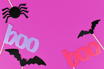 Halloween background with photo porps on sticks in shape of black bats and red and violet word 'boo' on pink background with copy space
