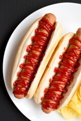 Tasty American Hot Dog with Potato Chips on a white plate on a black background, top view. Flat...