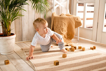 Little child boy plaing with wooden cube blocks on knitted carpet on the floor indoor. Knitted...