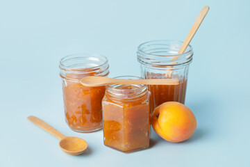 Jars of tasty apricot jam on color background