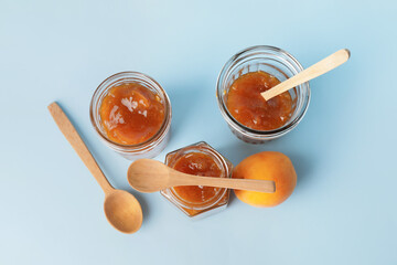 Jars of tasty apricot jam on color background