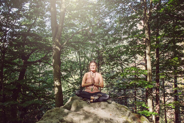 Fototapeta premium Woman in lotus position meditating on the rock in the forest