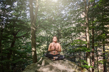 Woman in lotus position meditating on the rock in the forest