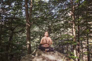 Fototapeta premium Woman in lotus position meditating on the rock in the forest