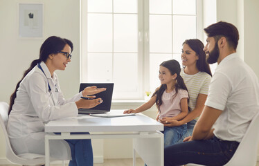 Family doctor. Young woman doctor consults parents with a little girl sitting at the table in the...