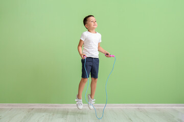 Cute little boy jumping rope near color wall