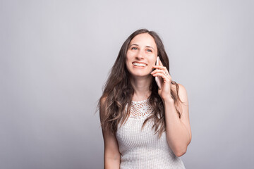 Photo of cute young woman talking on smartphone with someone over white wall