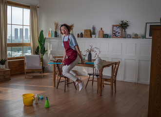 Happy woman/housemaid do the cleaning at home, she is happy and jumping on the mop