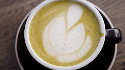 Top view of hand picking up coffee latte in black mug served on wooden table . Latte art