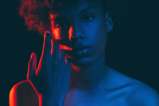 African Man Silhouette. Neon Light Portrait. Relaxed Black Guy In Blue Red Glow Touching Face With Hand Looking At Camera Isolated On Dark. Fashion Model. Aesthetic Cosmetology. Masculine Power