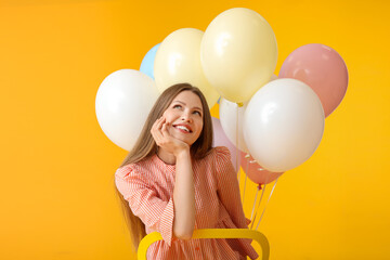 Young woman with balloons sitting on chair against color background