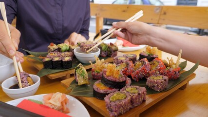 Two people eating delicious vegan sushi rolls, dipping into soy sauce at first. Healthy vegan street food