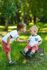 Naklejka na ściany i meble Children in green summer forest. Two little brothers on a wooden stump in spring park. Family walk outdoor. Friendly relationship in family. The same clothes