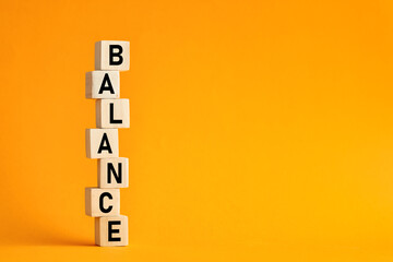 The word balance on wooden cubes with yellow background. Balance in life, work or business concept.