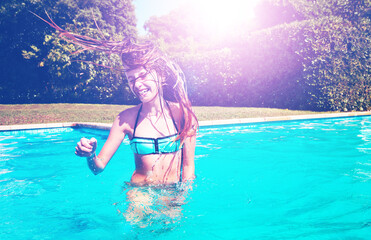 Happy dancing girl shake hair and head smiling standing in the swimming pool in the garden