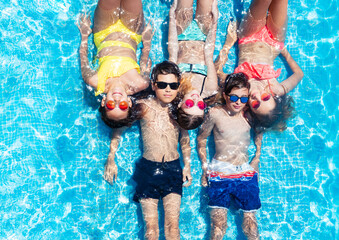 Group of kids lay in a row in the swimming pool water view from above in sunglasses