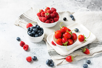 Ripe berries. Different berries in white ceramic bowls on a light table. Strawberries, raspberries and blueberries in plates against a white brick wall