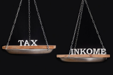 Balance between taxes and income. Balance scales on black background, close up