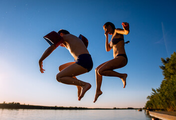 Single mother with her son enjoying on vacation jumping in lake from pier on summer day.