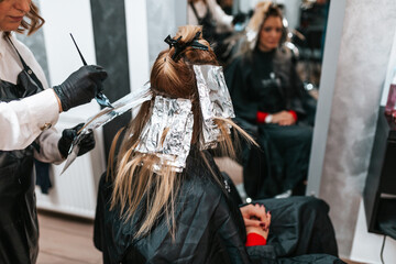 Fototapeta premium Hairdresser is dyeing female hair, making hair highlights to his client with a foil.
