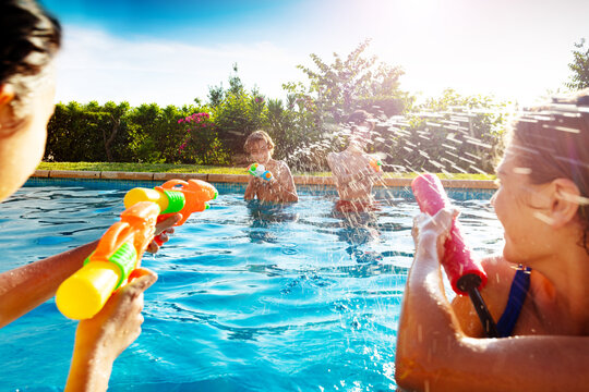 Group of kids in swimming pool shooting water-gun squirt pistol on sunny day