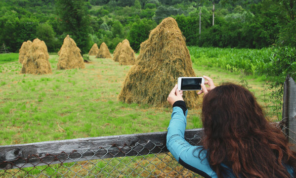 Turista fotografiando con su smartphone los montones de heno sobre estructuras de madera para secarse y evitar pudrirse en una granja de Curtea de Arges, Rumanía.
