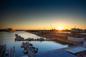 Sunset behind the sea and over a seaport with ships and port machinery. Valencia, Spain. With orange and blue colors