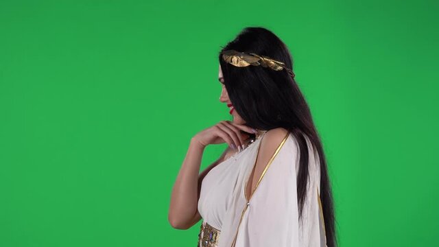 Portrait of beautiful woman in greek greece goddes dress and wreath high fashion is coquettishly smiling, waving hand and showing gesture come here. Side view. Green screen.