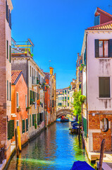 Fototapeta na wymiar Venice cityscape with narrow water canal with boats moored between old colorful buildings and stone bridge, Veneto Region, Northern Italy. Typical Venetian view, vertical view, blue sky background
