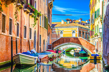 Fototapeta na wymiar Venice cityscape with gondolas and motor boats moored on narrow water canal near colorful buildings and stone bridge, Veneto Region, Northern Italy, blue sky in summer day, typical venetian view